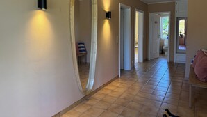 Een gang met een grote spiegel, inbouwverlichting en meerdere doorgangen naar andere kamers.