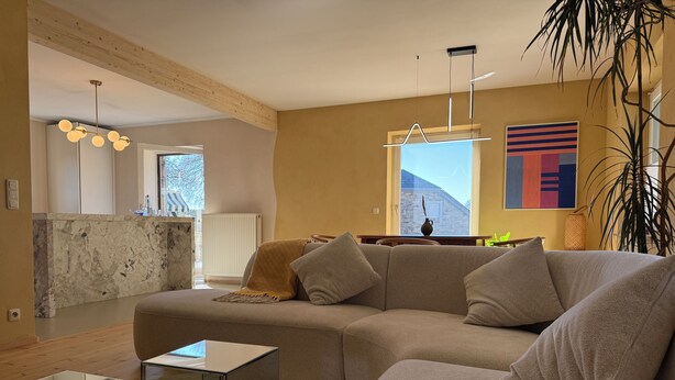 Een moderne woonkamer met een modulaire bank, een glazen salontafel, en een keuken op de achtergrond.