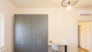 Una habitación moderna con un armario gris, un escritorio blanco, una silla y un radiador.