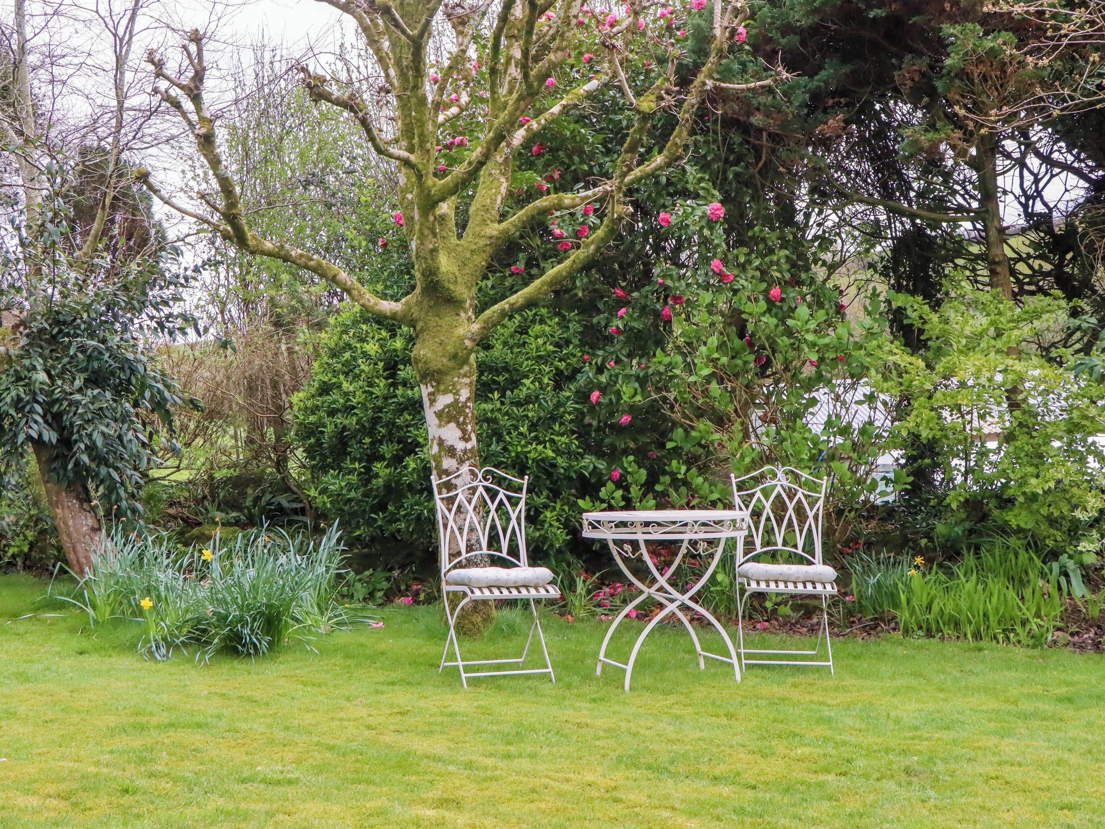 Ein Garten mit einem Metalltisch und -stühlen, umgeben von Grünpflanzen und blühenden Blumen.