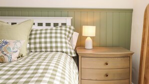 Een bed met geruit beddengoed, een nachtkastje met een lamp en een houten hoofdeinde.