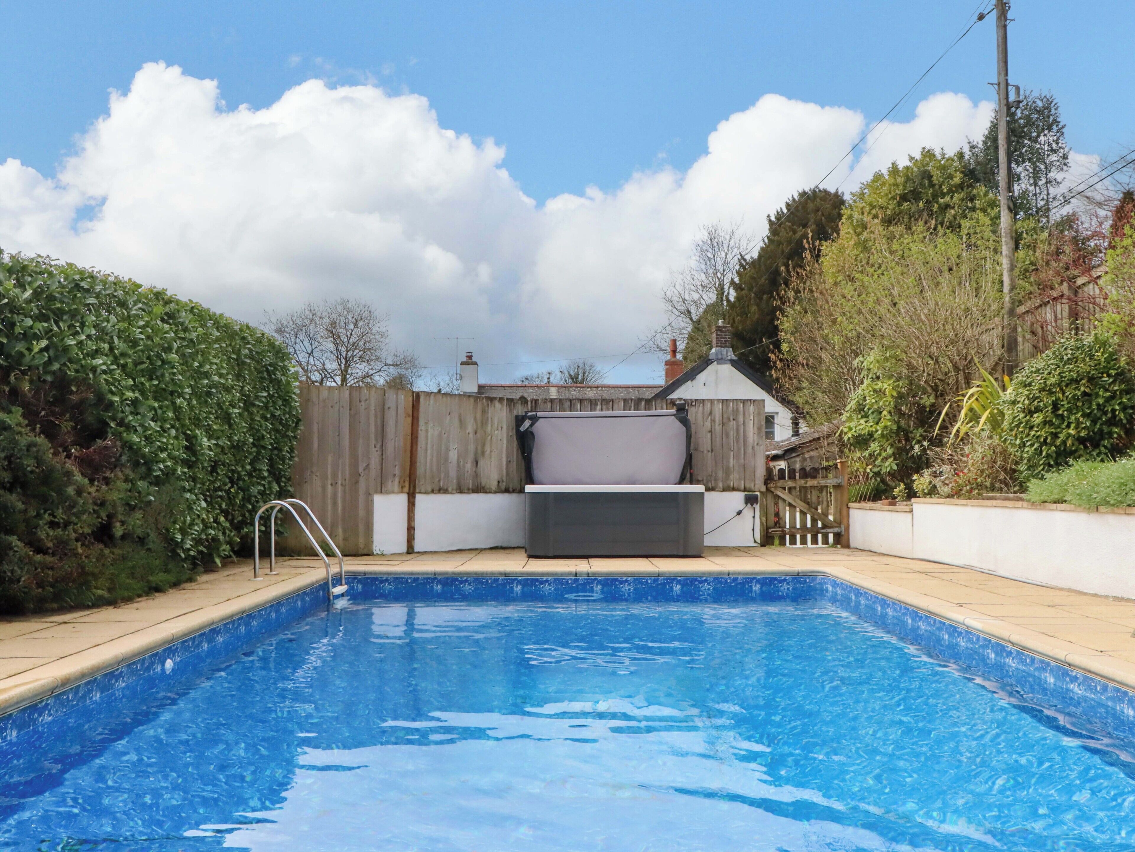 A swimming pool with a wooden deck, a metal ladder, and a white fence.