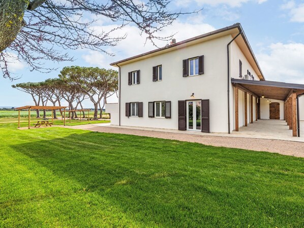 A modern two-story house with a covered patio, a well-maintained lawn, and a view of the countryside.