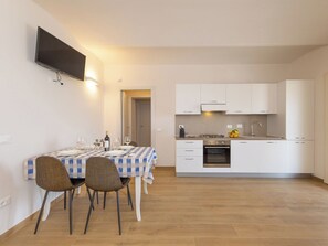 A modern kitchen with white cabinets, a built-in oven, and a dining area with a checkered tablecloth and chairs.