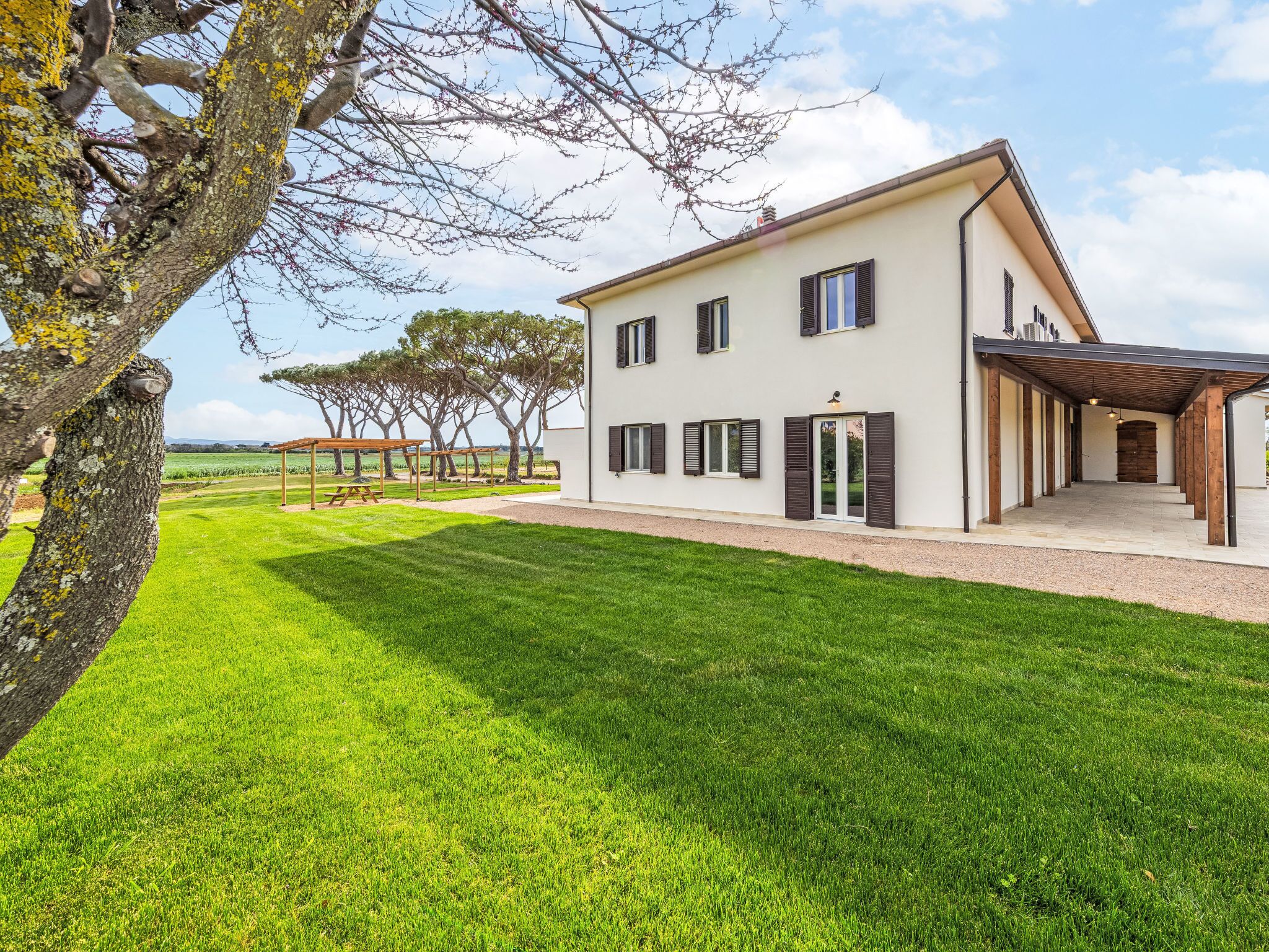 A modern two-story house with a covered patio, a well-maintained lawn, and a view of the countryside.