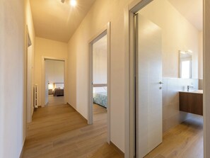 A hallway leading to a bedroom with a bed, a bathroom with a sink, and a mirror. - Apartment I Pini by Interhome (Bibbona)