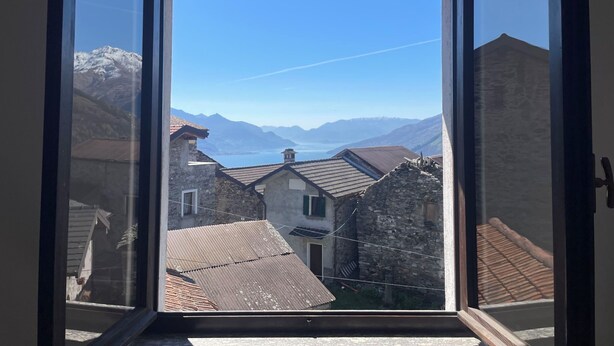 A view through a window of a mountain village with stone buildings and a clear sky. - Casa Pradell by Interhome (Gravedona)