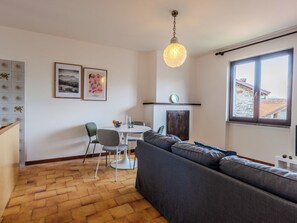 Ein Wohnzimmer mit einer Couch, einem Esstisch mit Stühlen, einer Hängeleuchte und einem Fenster mit Blick auf Gebäude.
