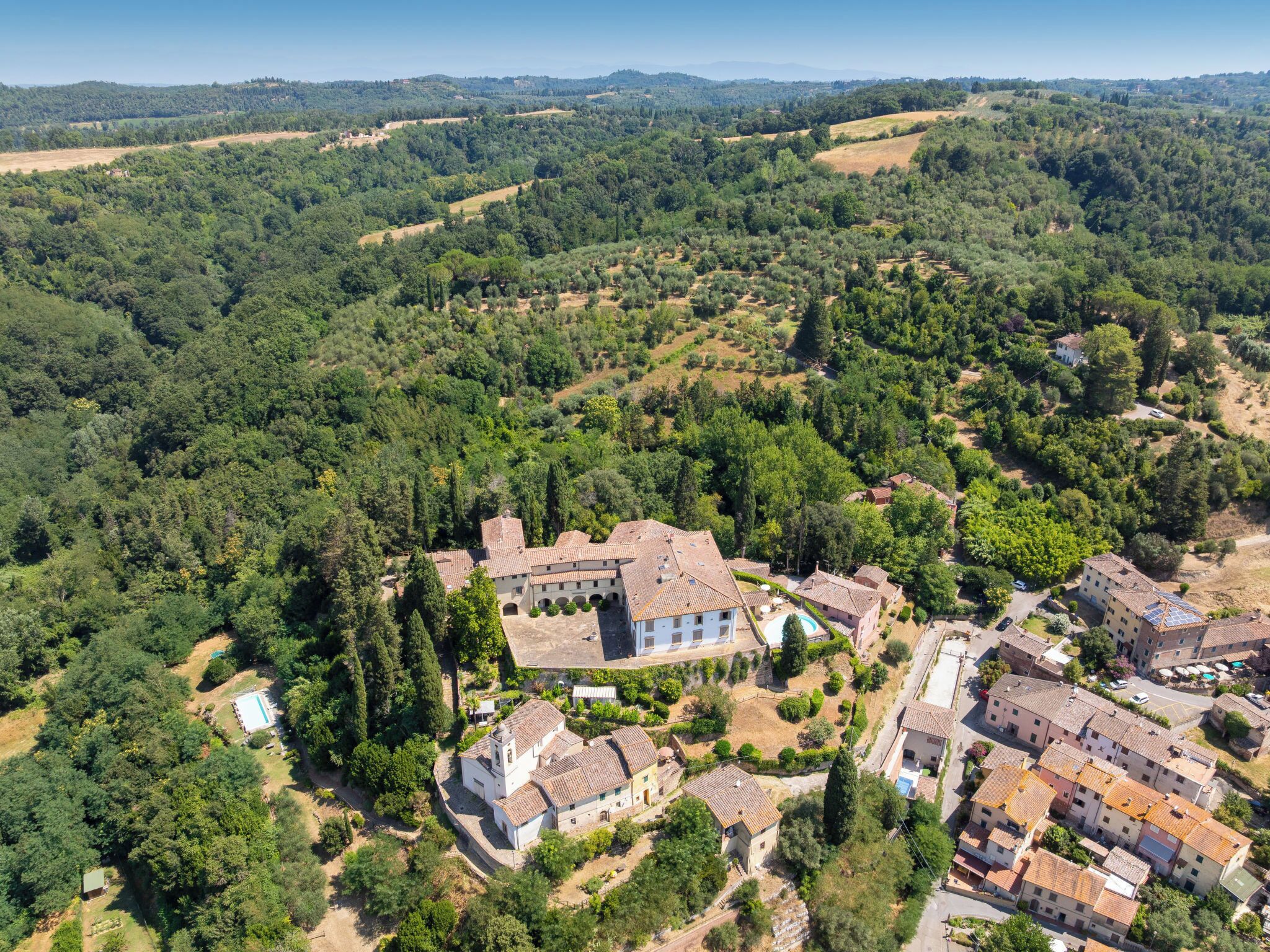 Una zona residencial con una amplia villa rodeada de árboles y casas más pequeñas.