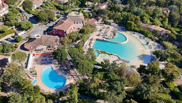 Vista aérea de un complejo turístico con dos piscinas grandes, un edificio central y abundante vegetación.