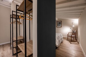 Una camera da letto con un letto, una sedia, un armadio con grucce e un quadro appeso al muro.