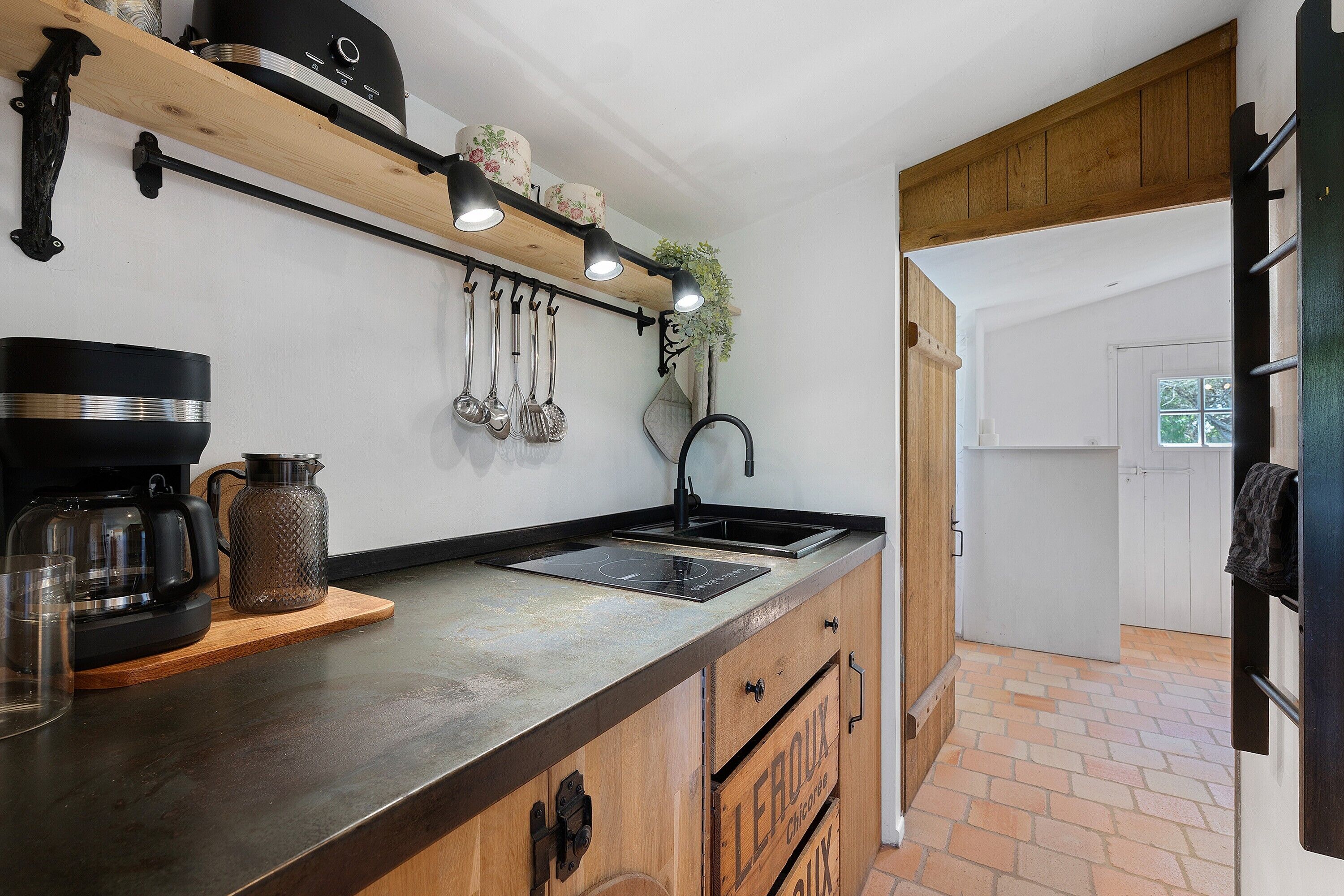A kitchen with a wooden countertop, a coffee maker, a kettle, and hanging utensils.
