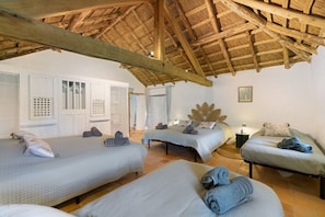 A room with three beds, a wooden ceiling, and a white wall with a picture.