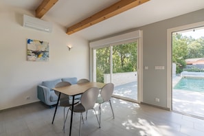 Un intérieur moderne comprenant une table à manger, des chaises, un canapé et une grande porte-fenêtre coulissante donnant sur un espace extérieur.