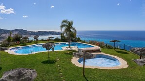 A pool area with two pools, a palm tree, and a view of the sea.