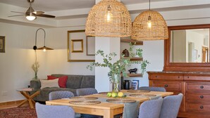 A dining area with a wooden table, grey upholstered chairs, woven pendant lights, and a modern ceiling fan.