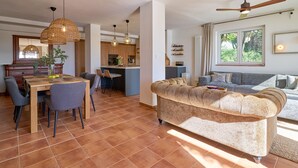 A spacious living area with a sofa, dining table, chairs, and a kitchen in the background.