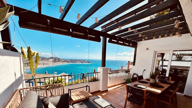 A balcony with a view of the sea, a dining area with a table and chairs, and a seating area with a sofa.