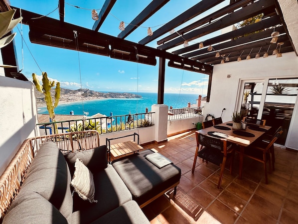 A balcony with a view of the sea, a dining area with a table and chairs, and a seating area with a sofa.