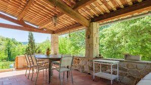 Eine Terrasse im Freien mit Holzboden, Steinwänden, einem Tisch mit Stühlen und Blick ins Grüne.