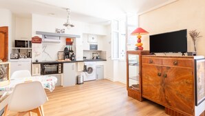 A modern kitchen with a microwave, oven, and washing machine, a dining area with a table and chairs, and a TV on a wooden cabinet. - Apartment 'T2 Océane' with Wi-Fi (Salies-de-Béarn)