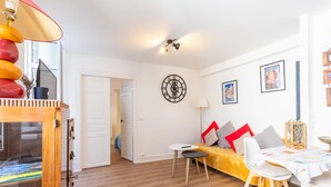 A living room with a sofa, a small table, a clock on the wall, and a door leading to another room. - Apartment 'T2 Océane' with Wi-Fi (Salies-de-Béarn)