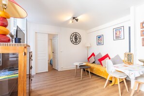 Ein Wohnzimmer mit Sofa, einem kleinen Tisch, einer Wanduhr und einer Tür zu einem anderen Raum.