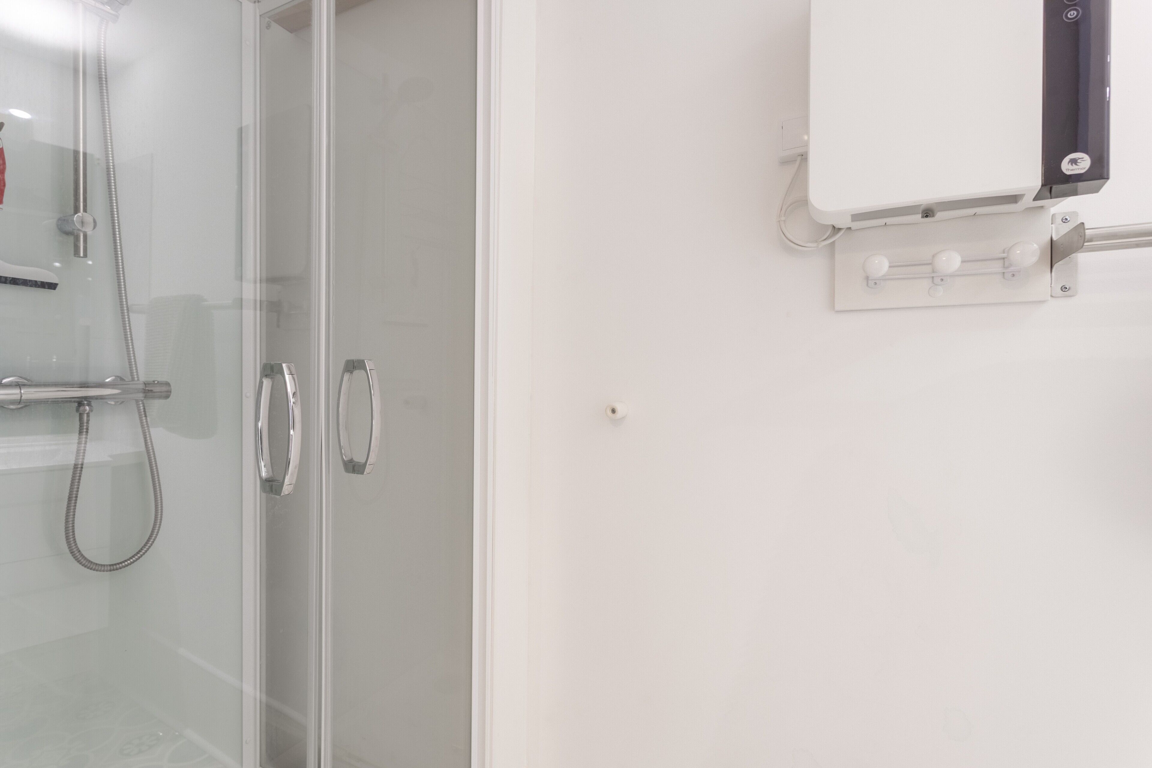 A bathroom with a glass shower enclosure, a white wall-mounted heater, and a control panel.