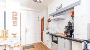 A compact kitchen with a white refrigerator, a stove, and a coffee maker on the counter. - Apartment 'T2 Océane' with Wi-Fi (Salies-de-Béarn)