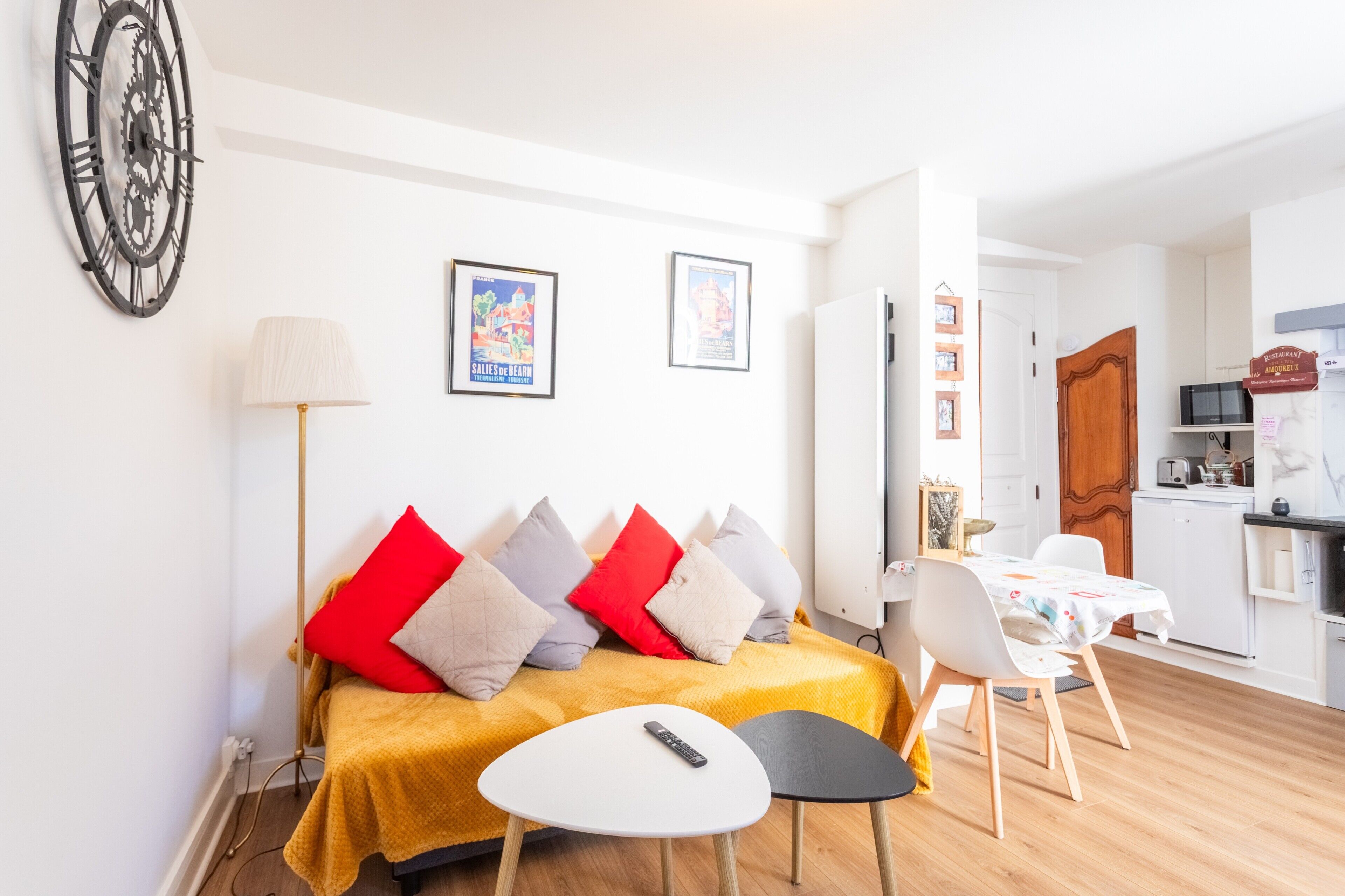 Un salon avec un canapé, une petite table, une lampe et, au fond, un coin cuisine.
