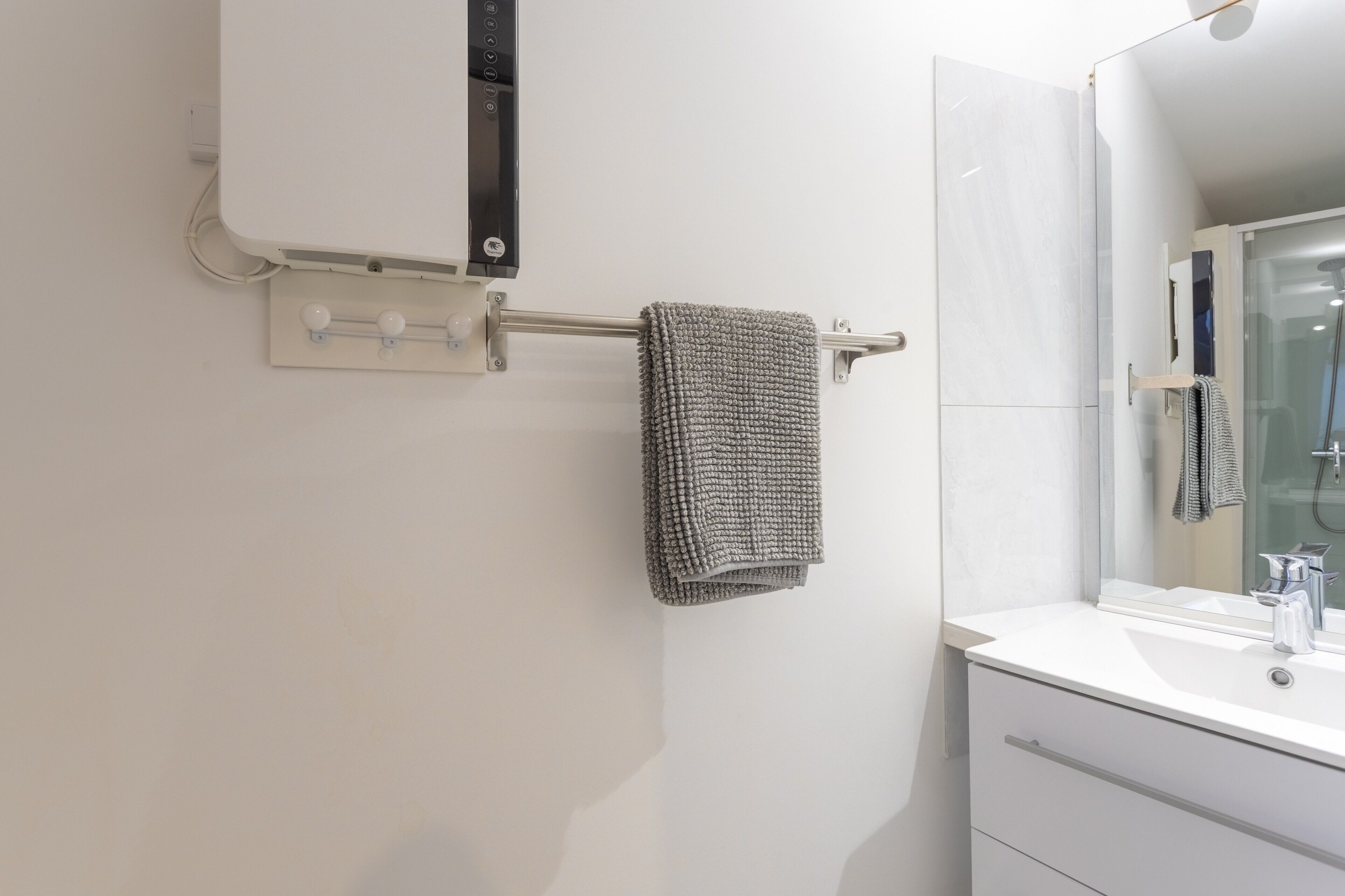 Une salle de bain avec un lavabo blanc, une serviette suspendue à un porte-serviettes et un miroir au-dessus du lavabo.
