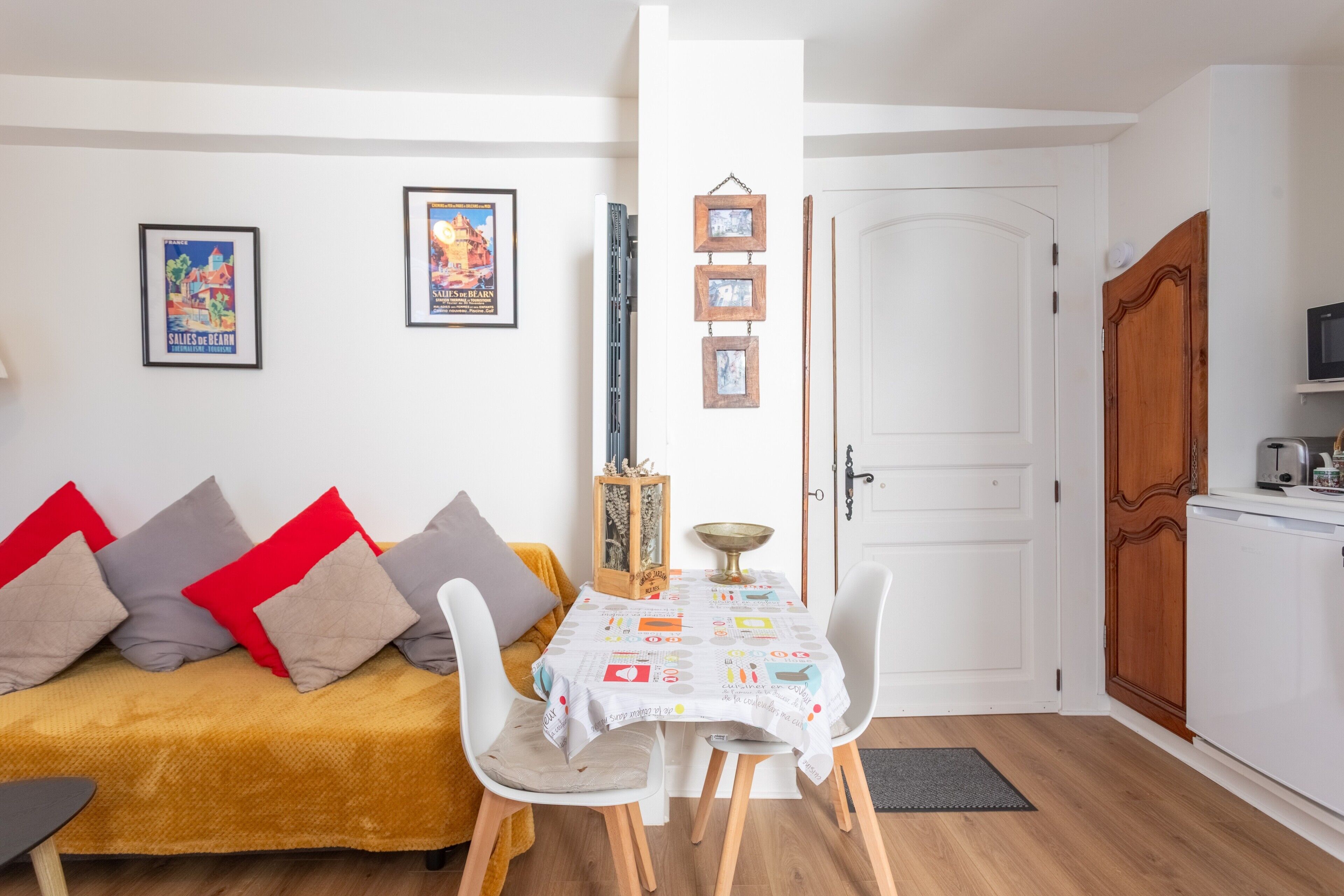 A compact living space with a sofa, dining table, chairs, a kitchen area, and a door.