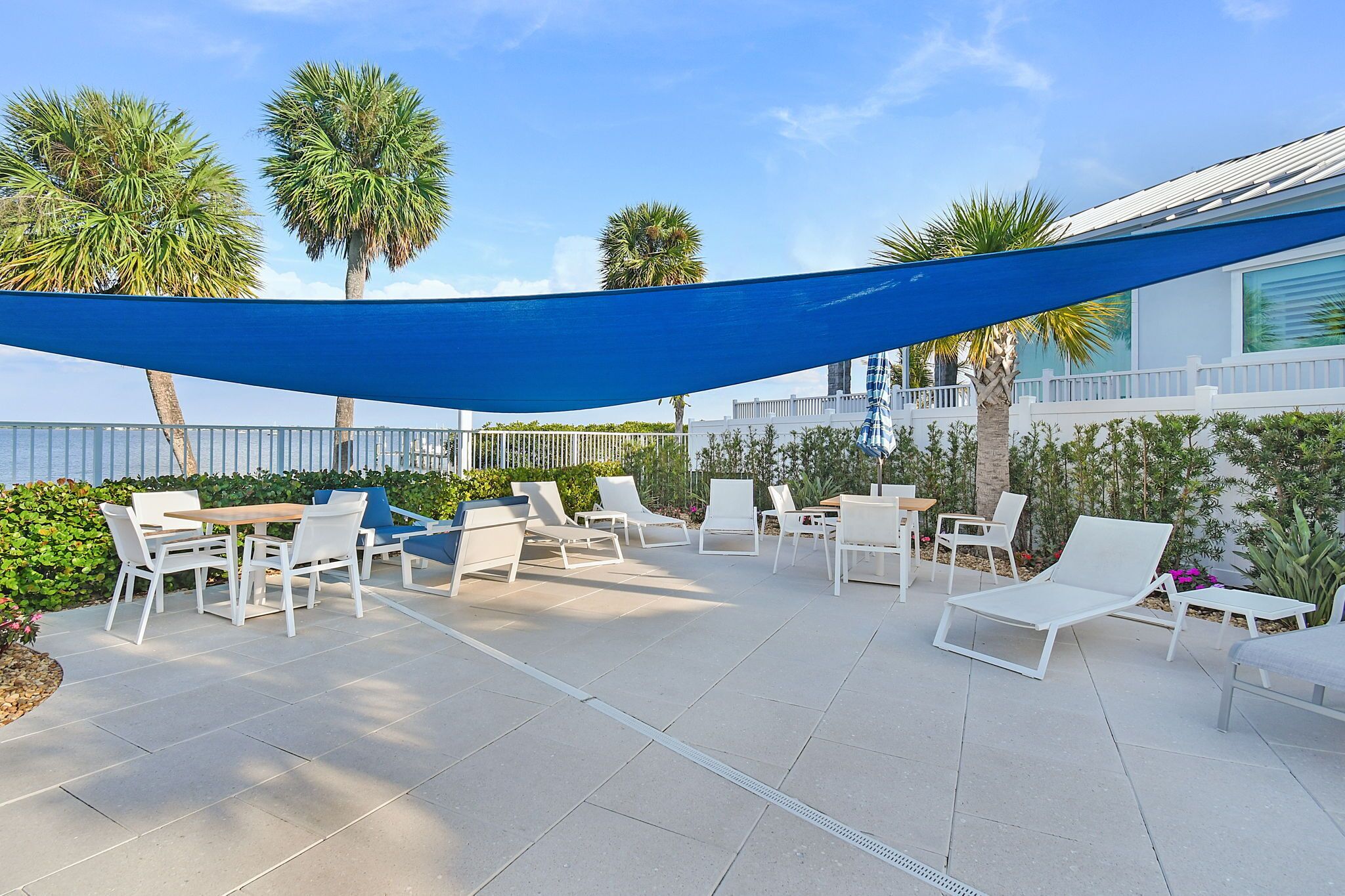 Eine Terrasse mit weißer Möbel, einem blauen Sonnensegel und Palmen.