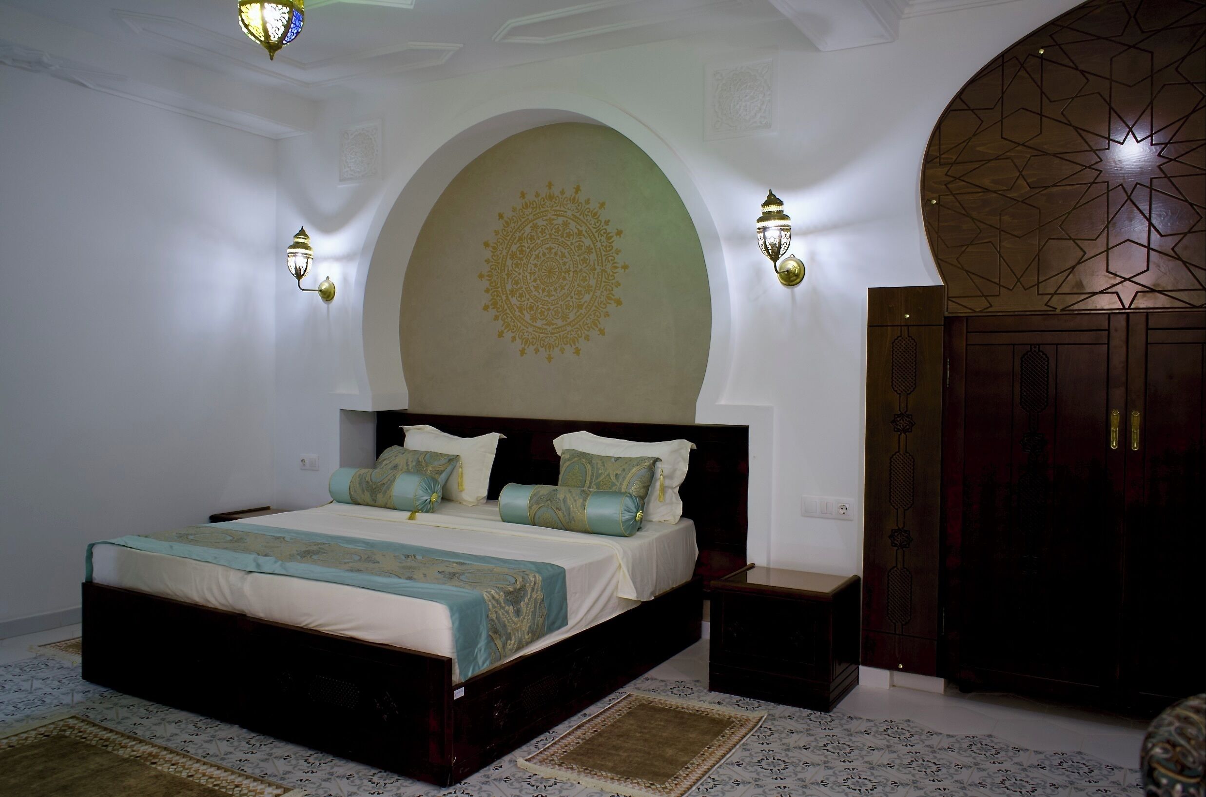 A bedroom with a large bed, two wall sconces, a decorative ceiling medallion, and a wooden wardrobe.
