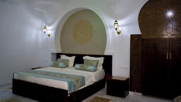 A bedroom with a large bed, two wall sconces, a decorative ceiling medallion, and a wooden wardrobe.