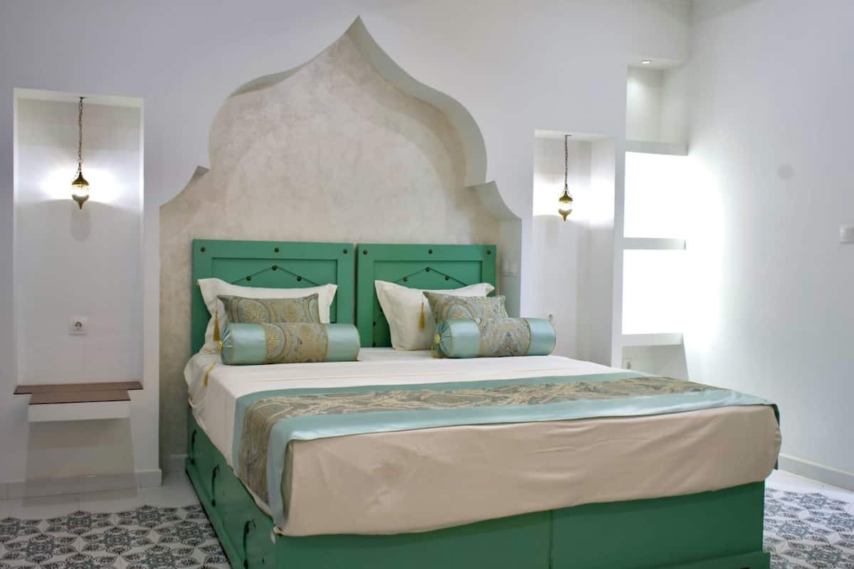 A bedroom with a green headboard, a bed with multiple pillows, and two wall-mounted light fixtures.