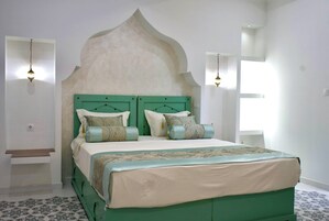 A bedroom with a green headboard, a bed with multiple pillows, and two wall-mounted light fixtures.