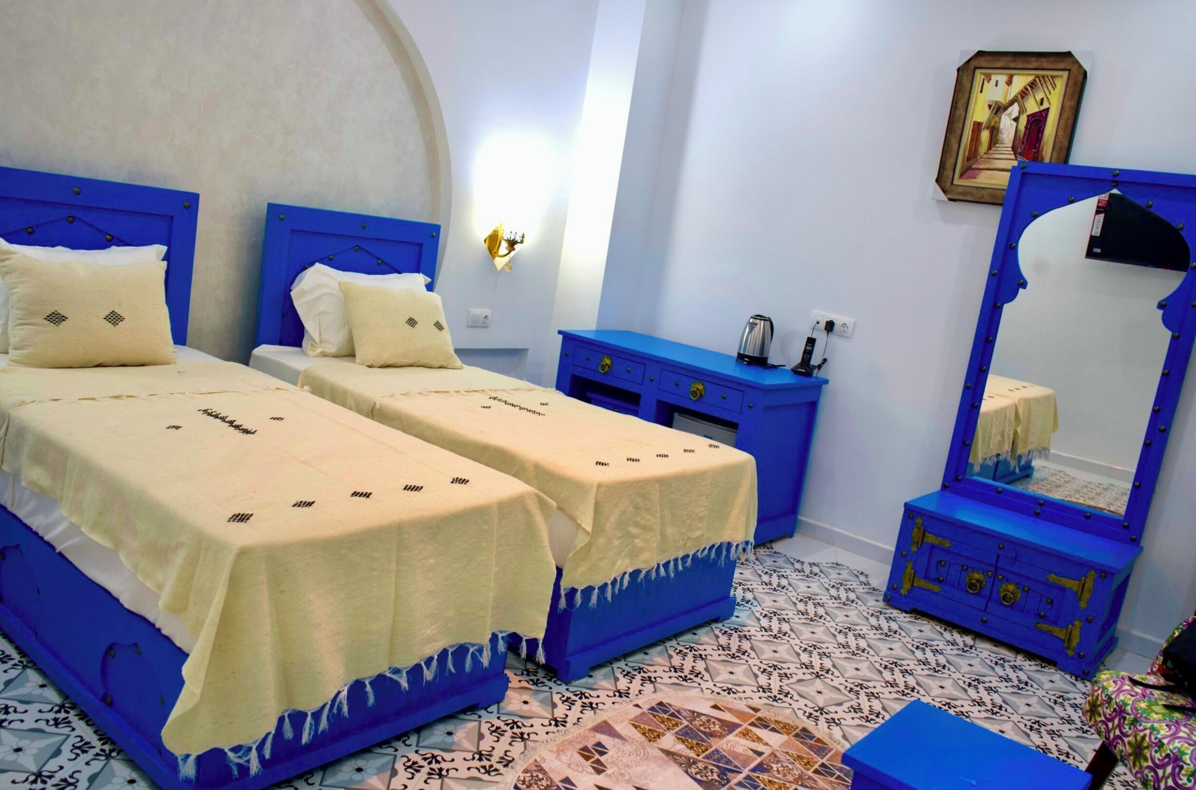 A room with two beds, a blue dresser, a mirror, and a patterned floor.