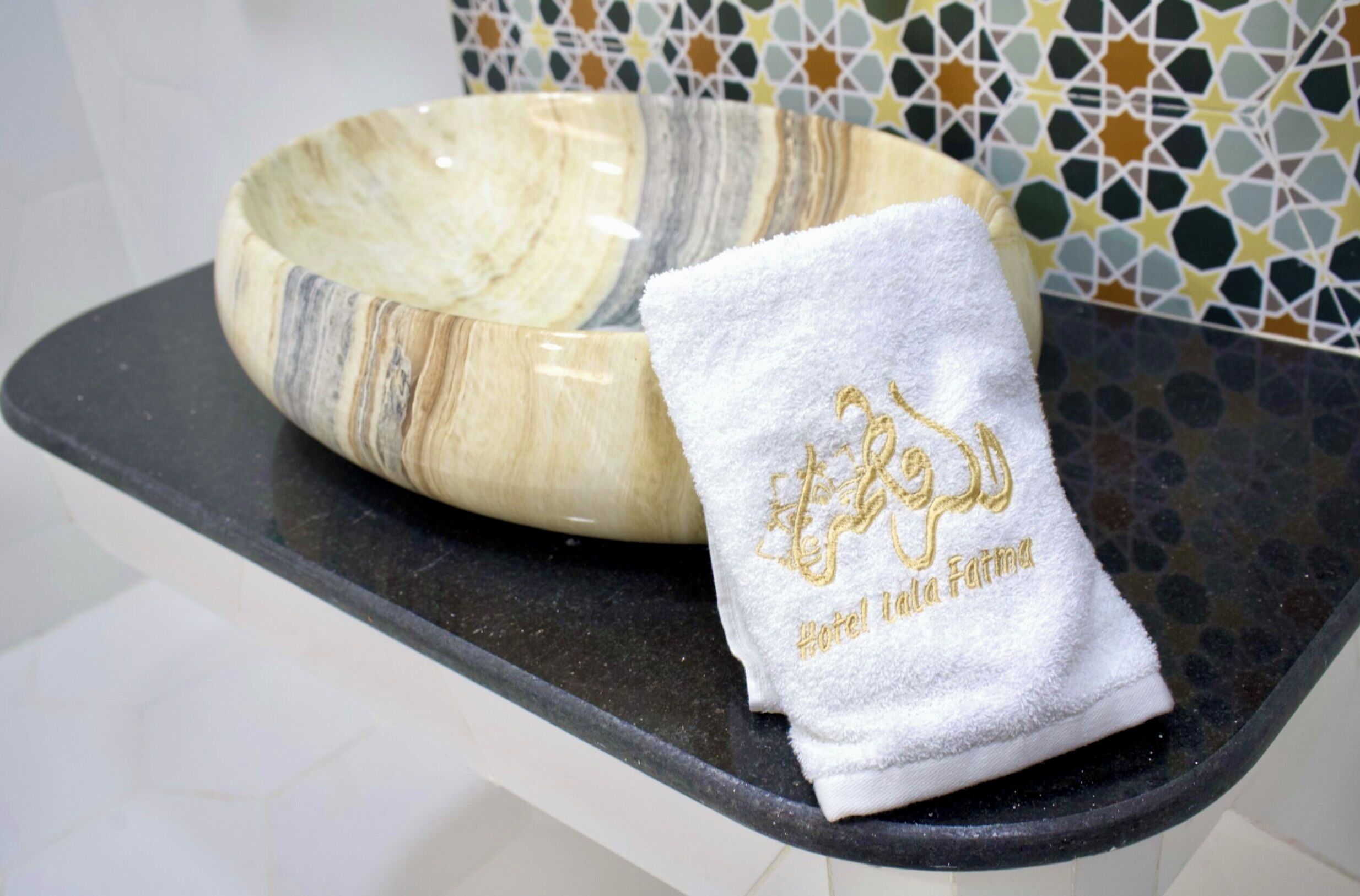 A marble bowl and a white towel with gold embroidery on a black countertop.