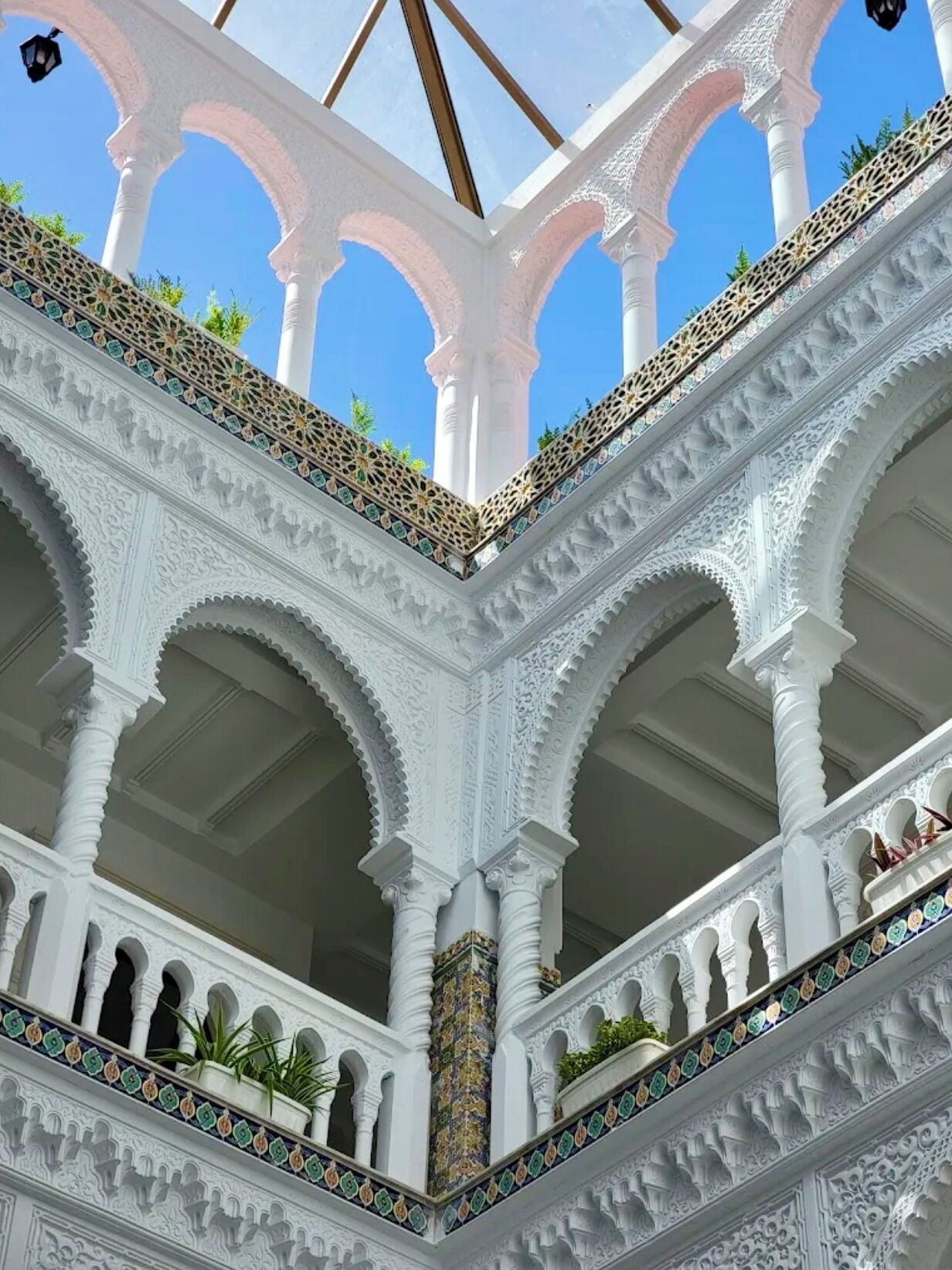 A multi-level structure with ornate white columns and arches, featuring intricate tile work and potted plants.