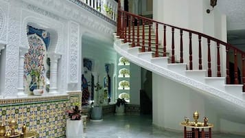 Um interior imponente com piso de mármore, uma fonte central e uma escadaria com grades brancas.