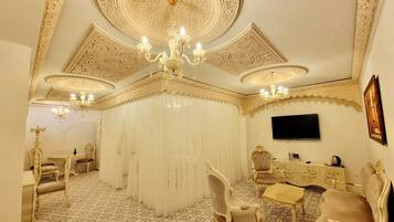 A room with ornate ceiling designs, chandeliers, patterned flooring, and classic furniture.