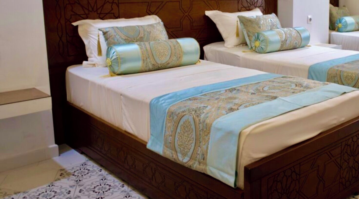 Deux lits doubles avec des couvre-lits et des coussins assortis à motifs, une tête de lit en bois et un tapis à motifs.