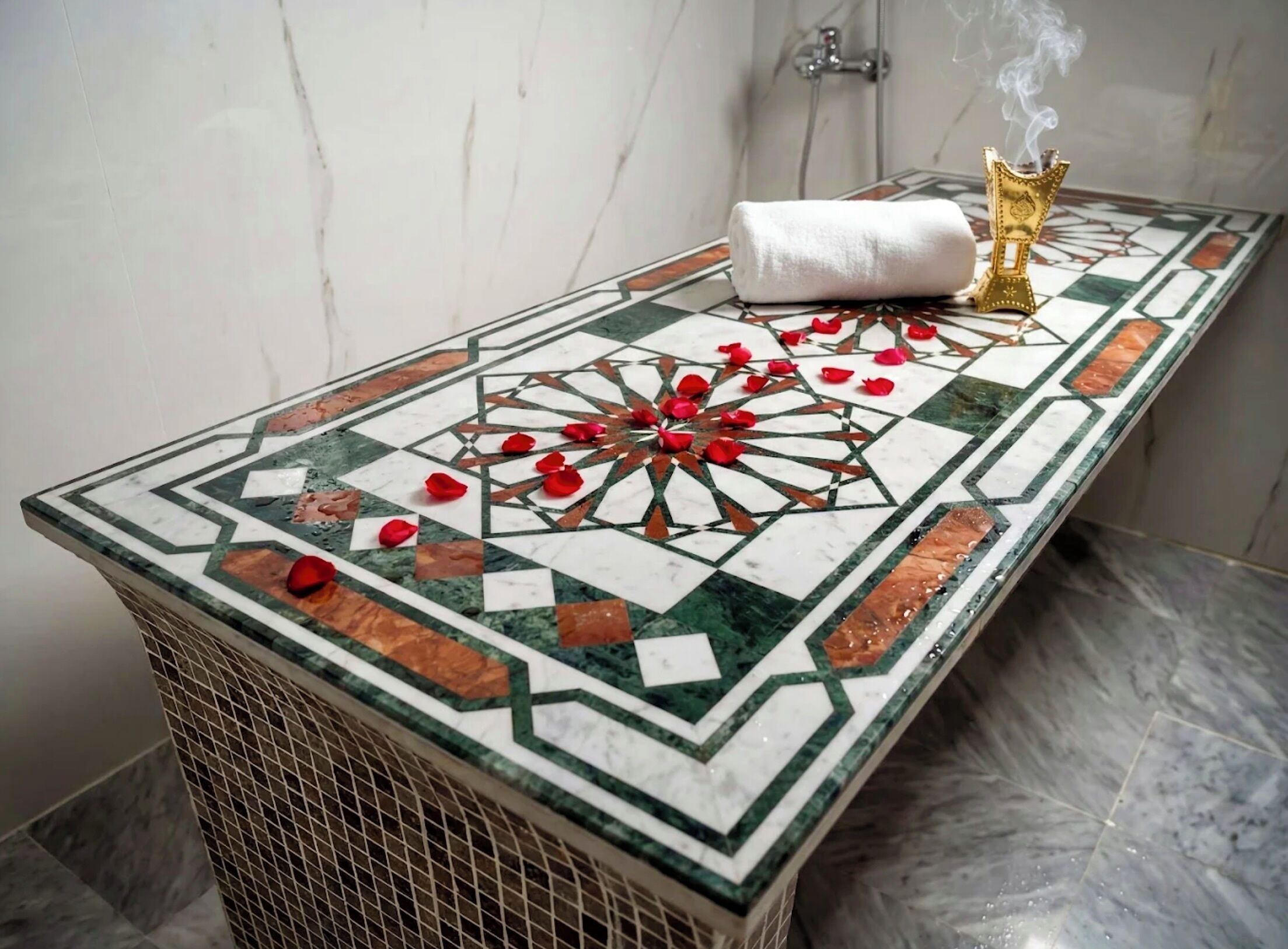 A bathroom with a tiled floor, a towel, rose petals, and a golden candelabra.