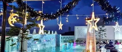 Un área de piscina interior decorada con una fuente, plantas en macetas y luces colgantes.
