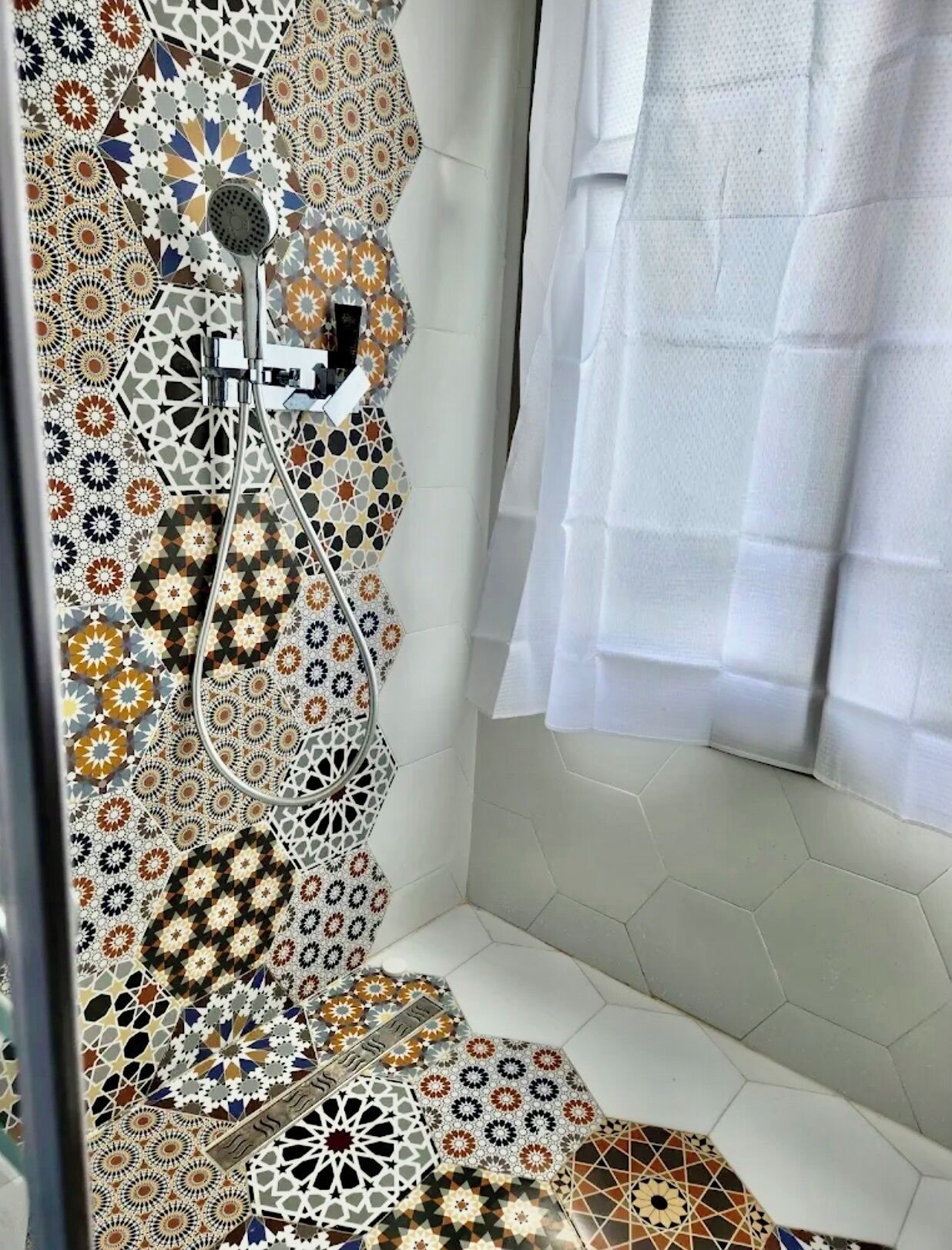 A bathroom with a shower, a white curtain, and patterned tiles.