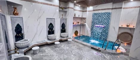 Un baño lujoso con pisos de mármol, varios lavamanos, una bañera grande y una cascada decorativa.