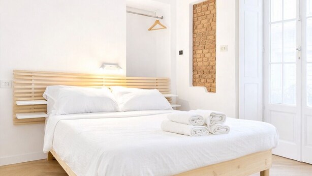 Een minimalistische slaapkamer met een houten bed, witte beddengoed en een wand van baksteen.