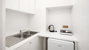 Een kleine keuken met witte kastjes, een roestvrijstalen spoelbak, een waterkoker, een broodrooster en een kleine koelkast.