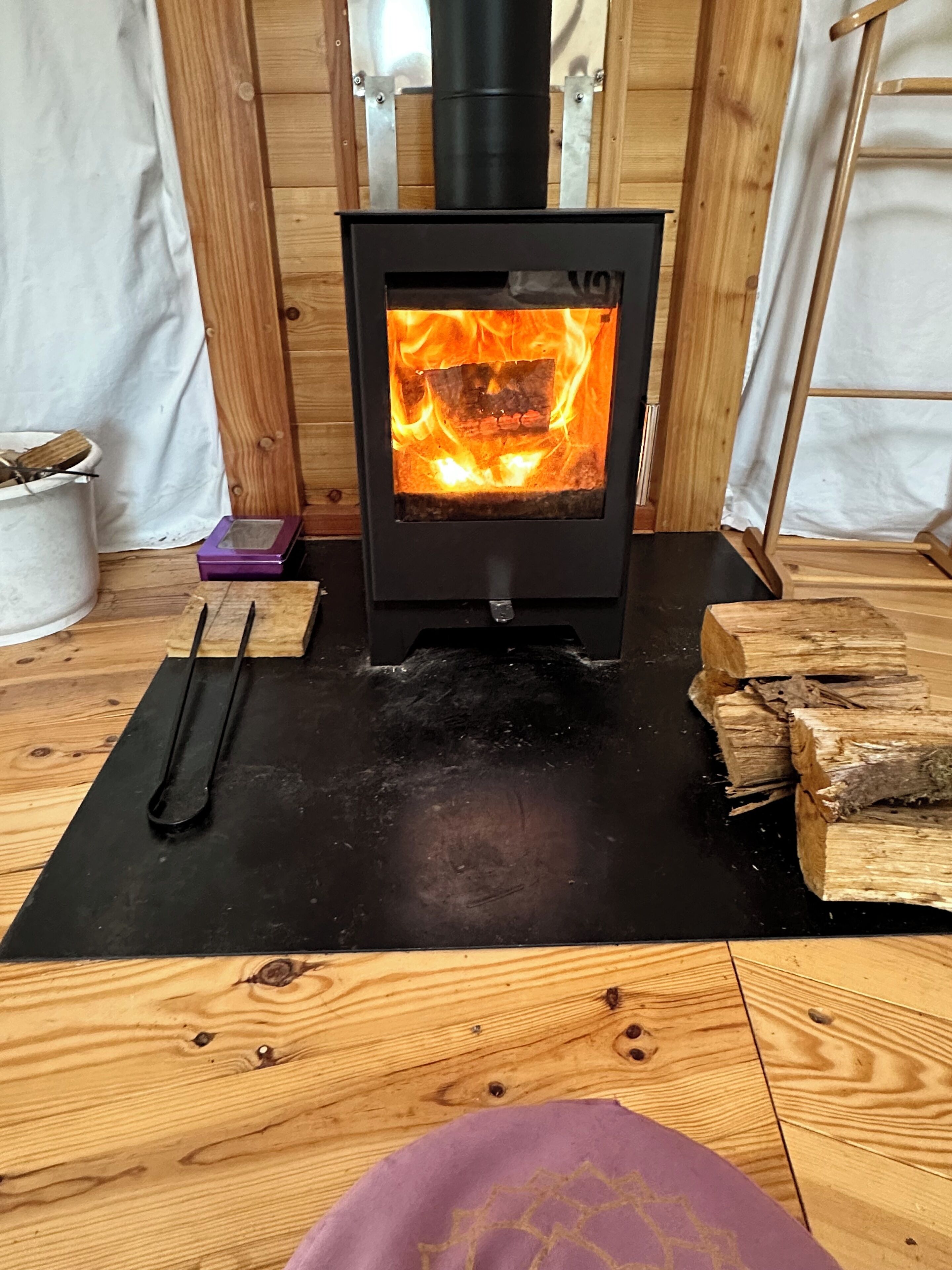 En vedeldad kamin med synliga lågor, en svart matta och staplade vedträn.